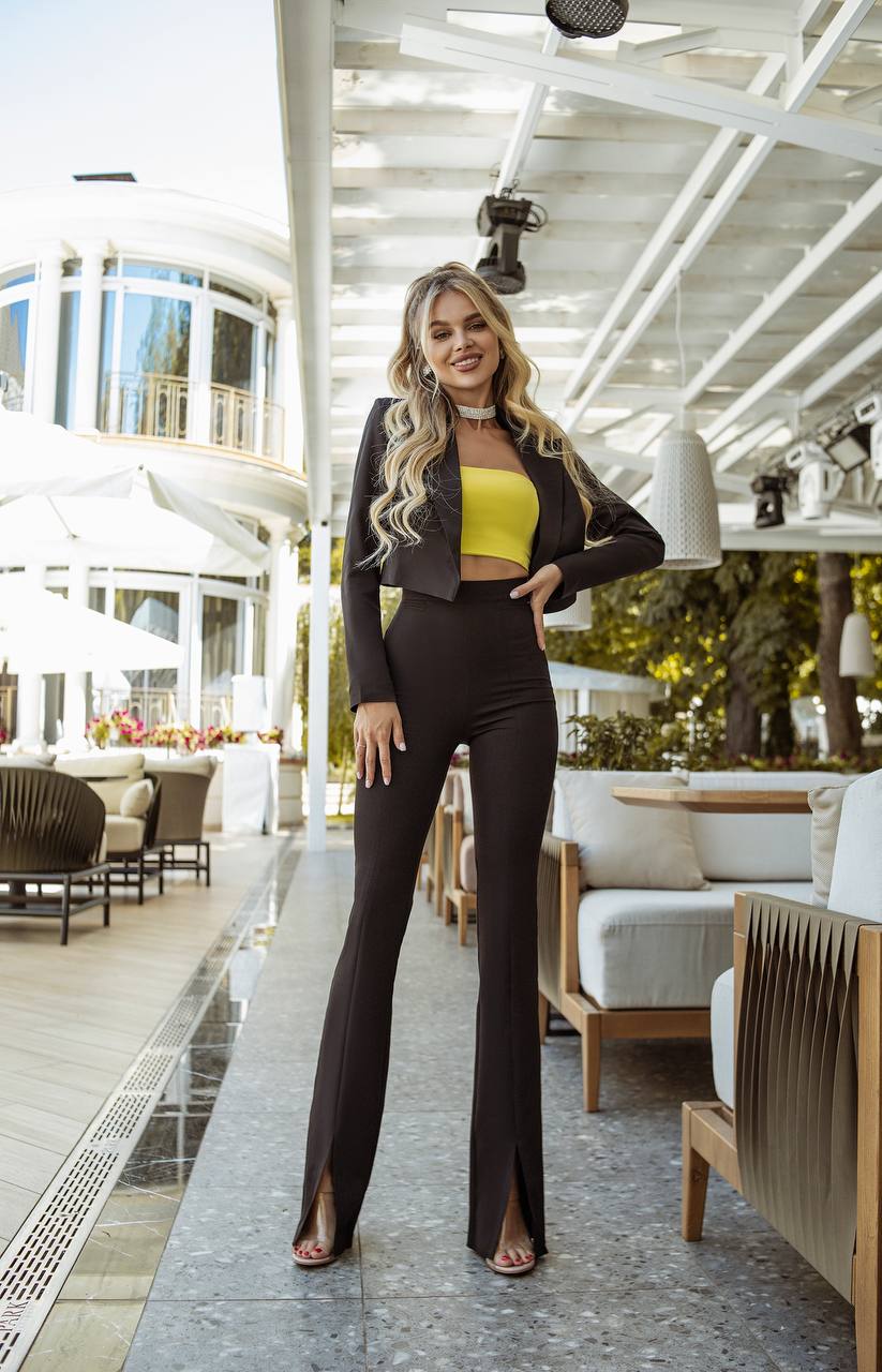 Woman in a black outfit with a yellow top standing in an outdoor setting.