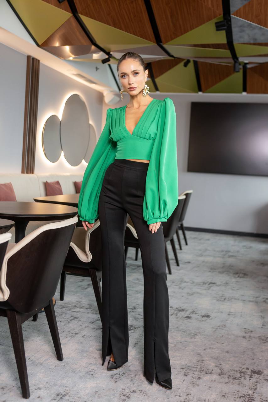 Woman in a green top and black pants standing in a modern restaurant setting.