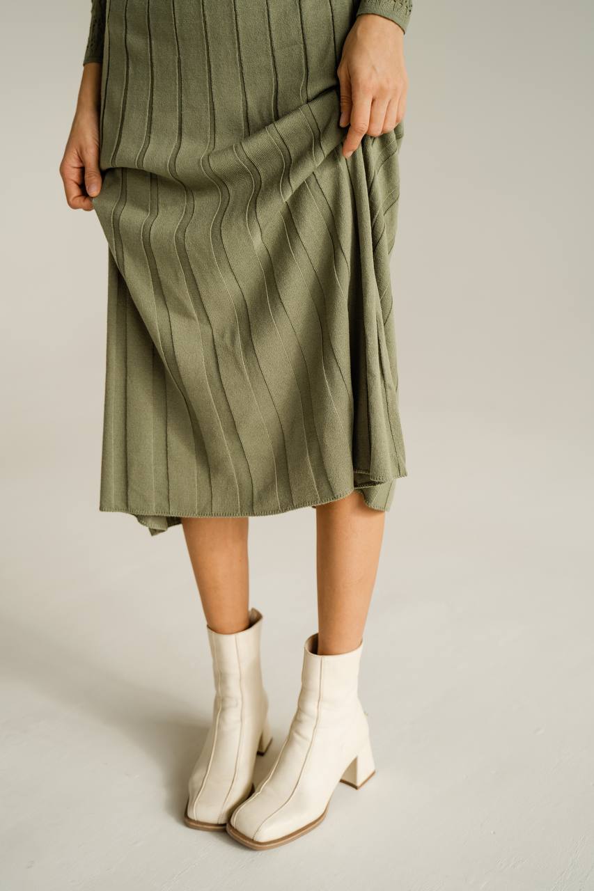 Person wearing a green ribbed dress and white boots on a plain background