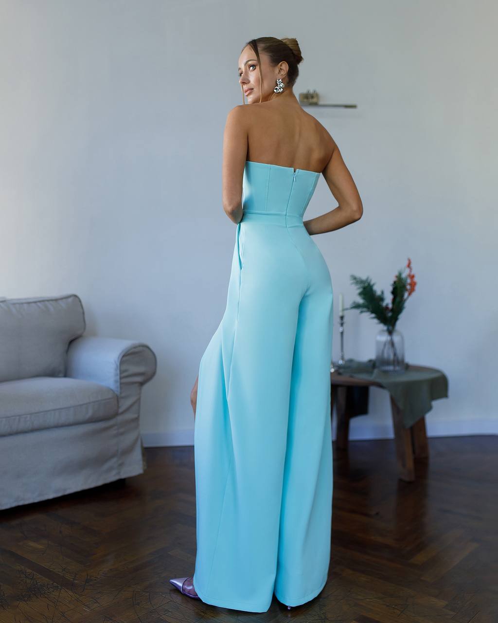Woman wearing a light blue strapless jumpsuit in a living room setting.