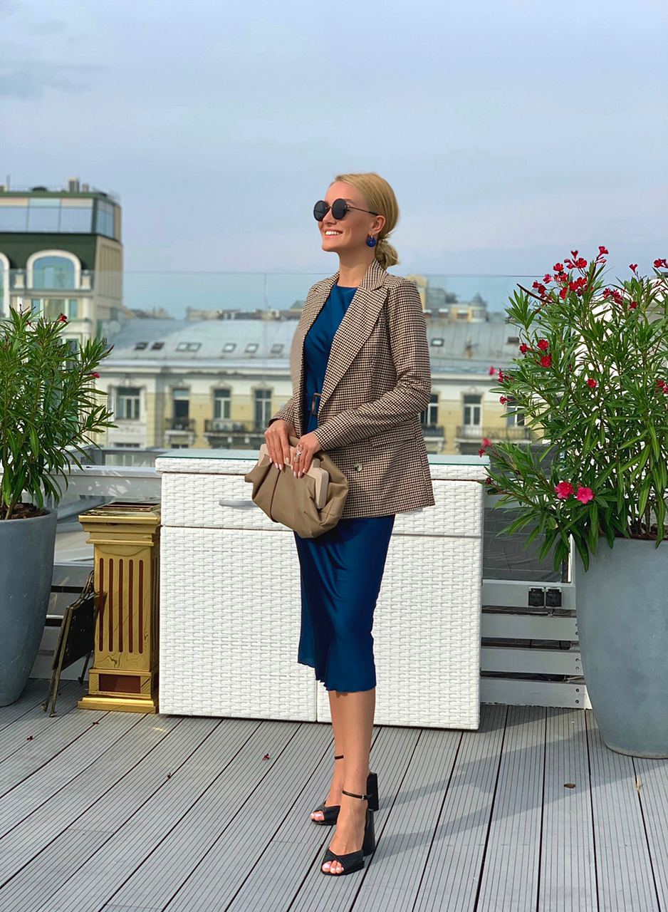Woman in a stylish outfit on a rooftop with plants and cityscape in the background