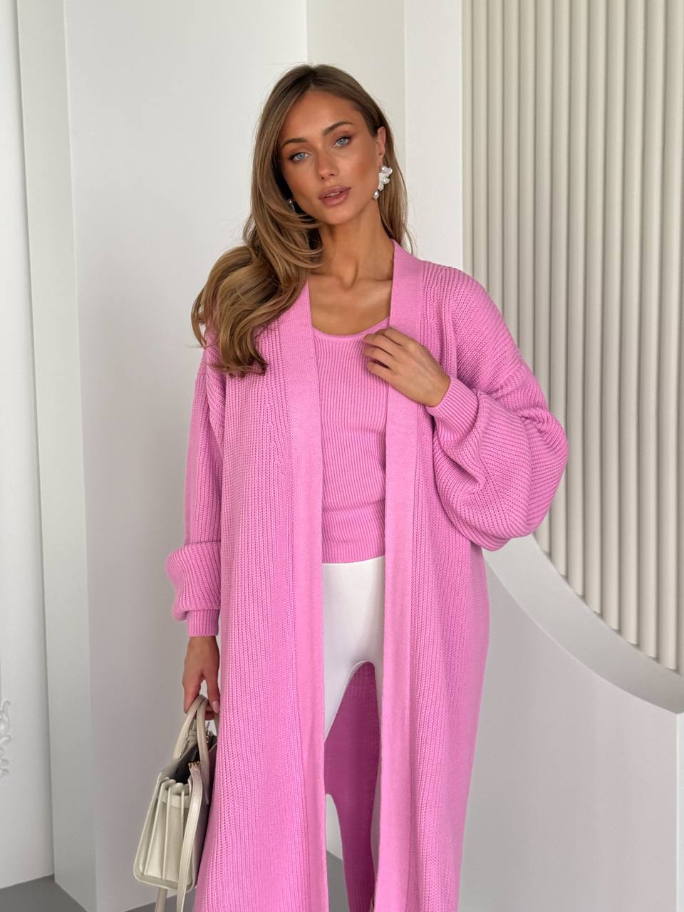 Woman wearing a pink outfit with a long cardigan and matching top, standing against a white background.
