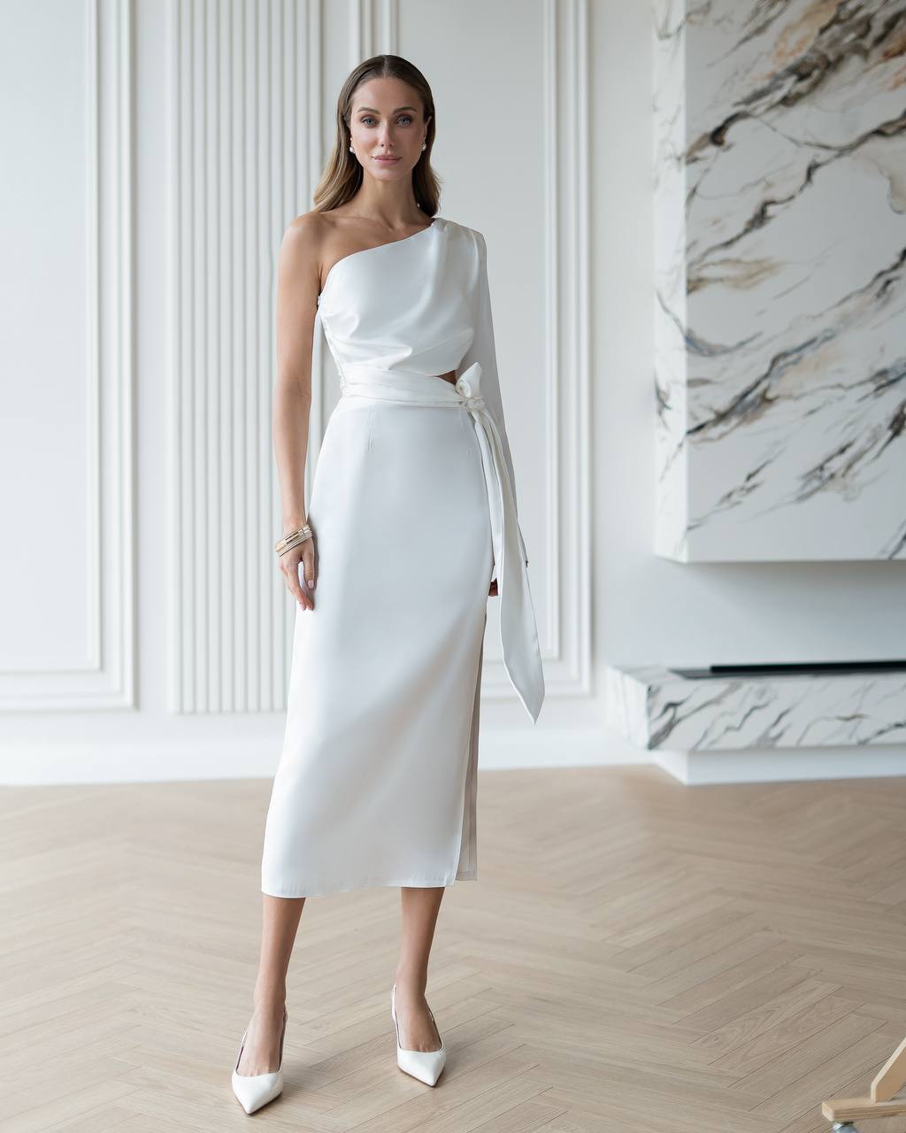Woman wearing a white one-shoulder dress in an elegant interior setting.