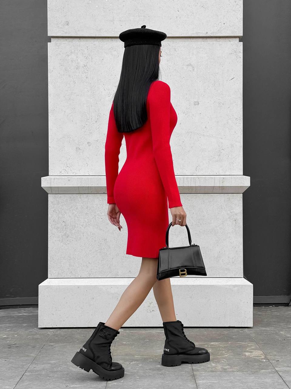 Person wearing a red dress and black beret holding a black handbag, walking on a gray pavement.