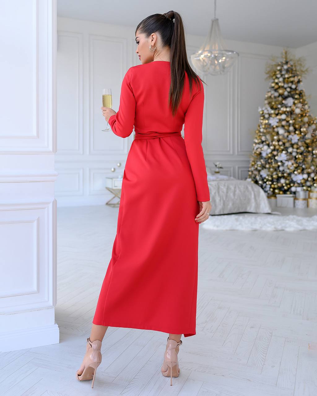 Woman in a red dress holding a glass in a room with a decorated Christmas tree.