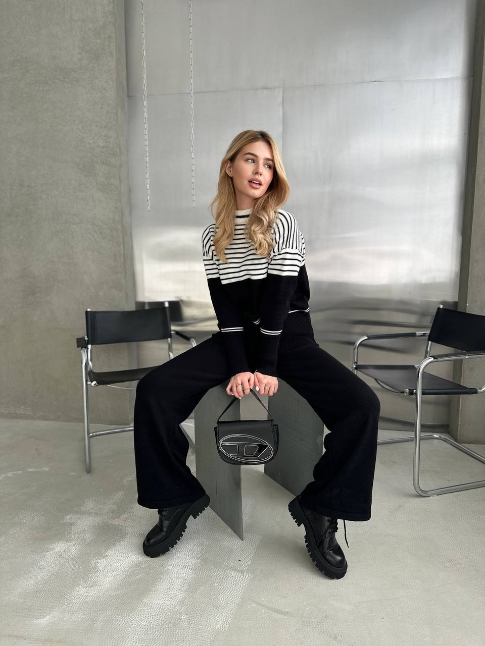 Woman sitting on a modern chair in a minimalistic room with metallic walls.