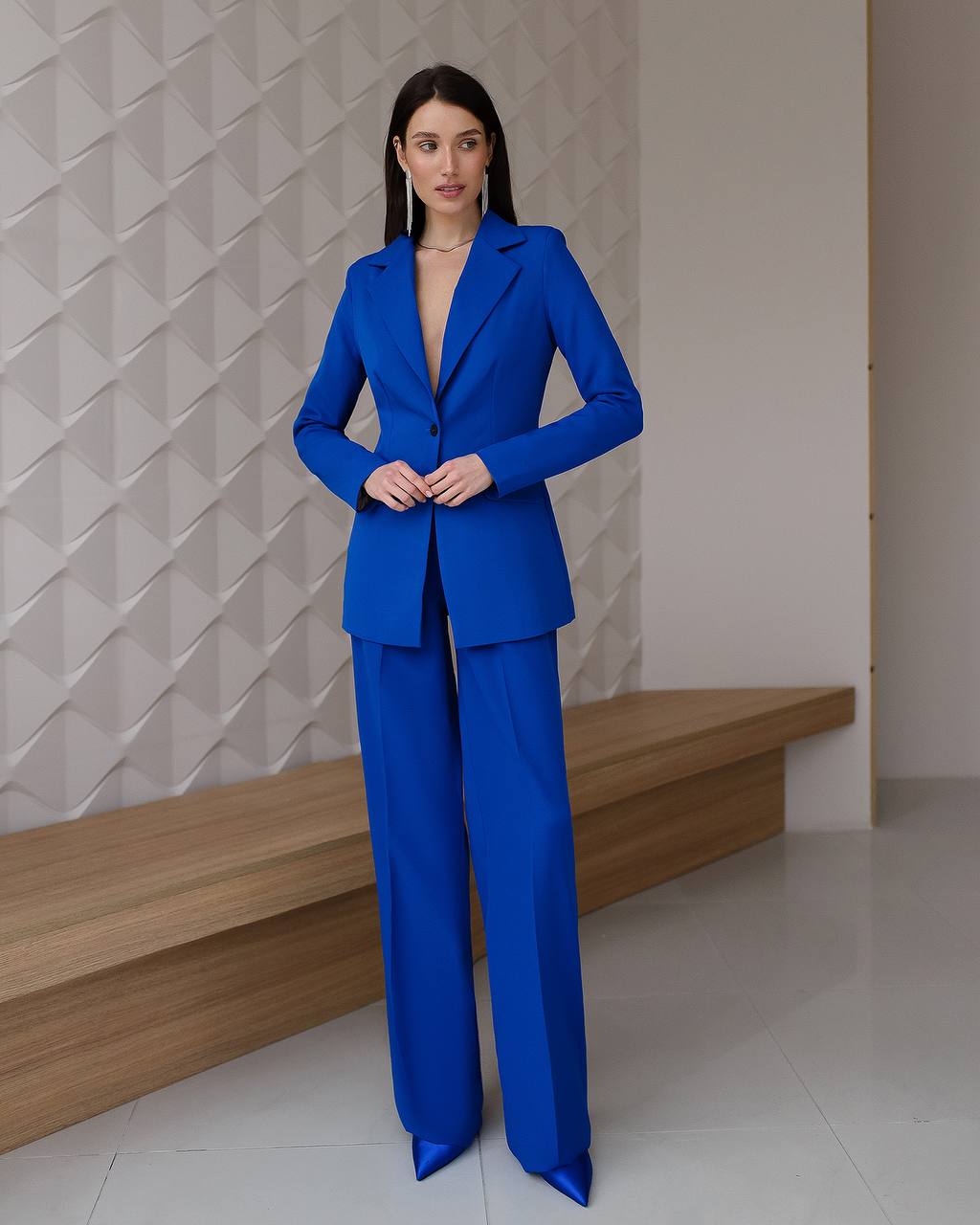 Woman wearing a blue suit standing against a geometric-patterned wall.