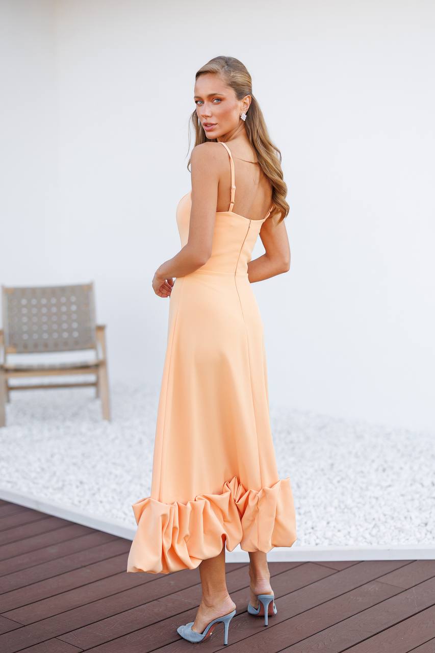 Woman in a peach dress standing on a wooden deck with a white wall background