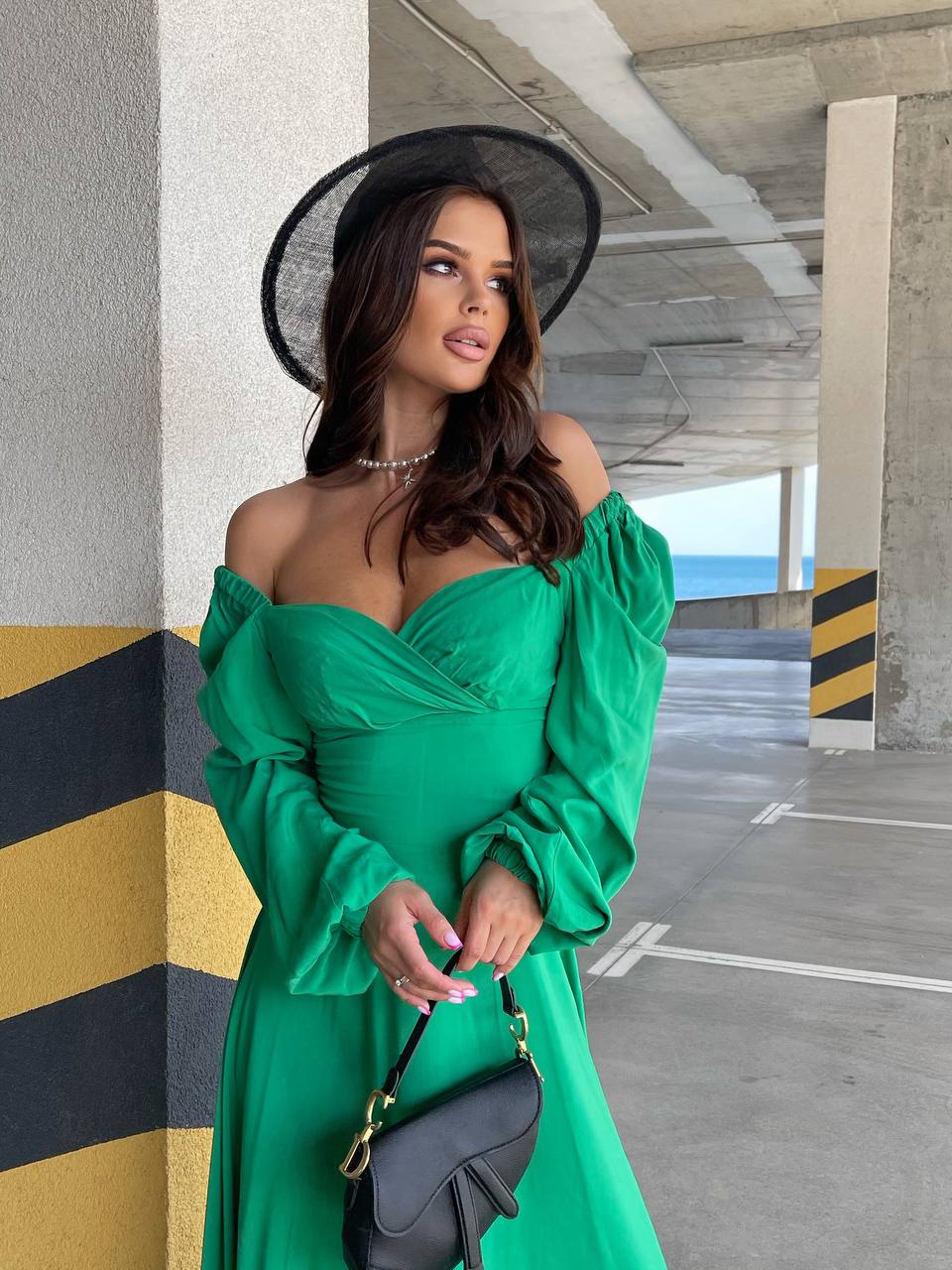 Woman in a green dress and black hat standing in an urban setting.