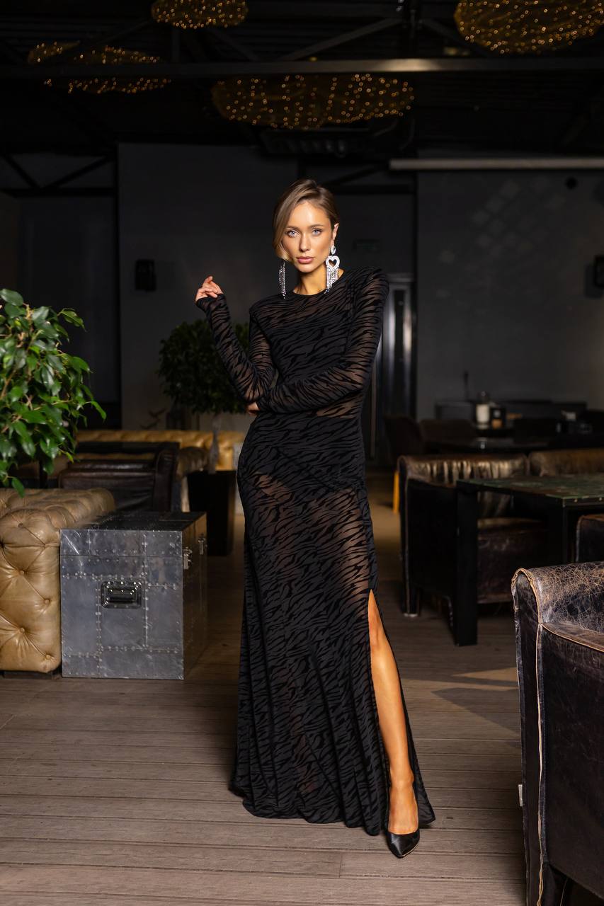 Woman in a black evening gown with a high slit standing in an elegant indoor setting.