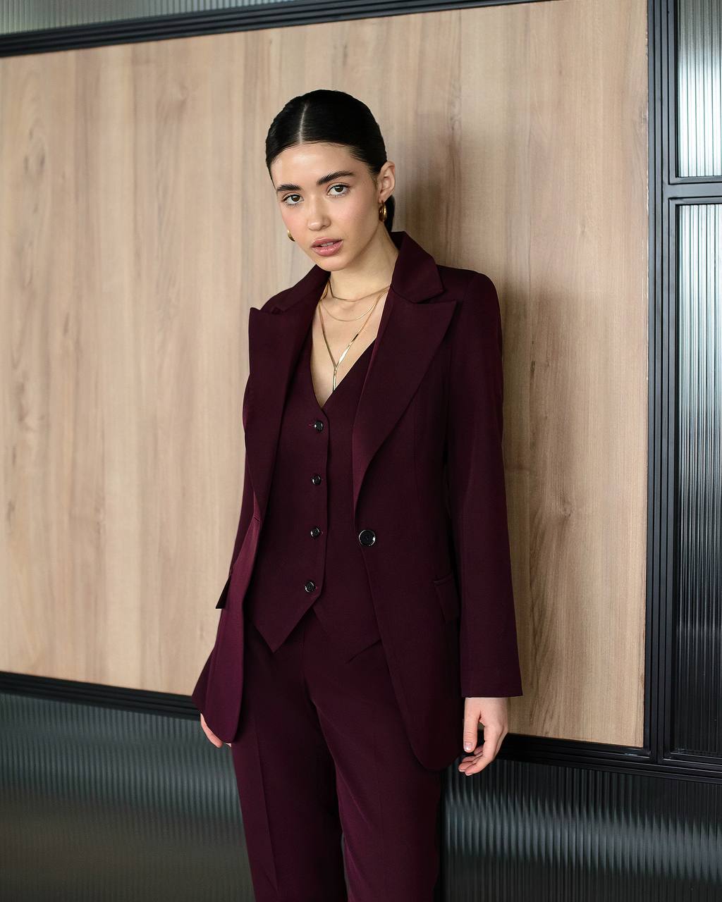 Woman in a burgundy suit standing against a wooden wall.
