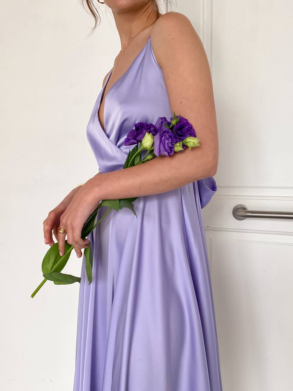 Woman in a lavender dress holding a bouquet of purple flowers against a white background