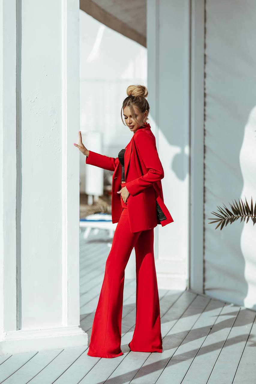 Woman in a red outfit standing on a wooden deck with white columns.