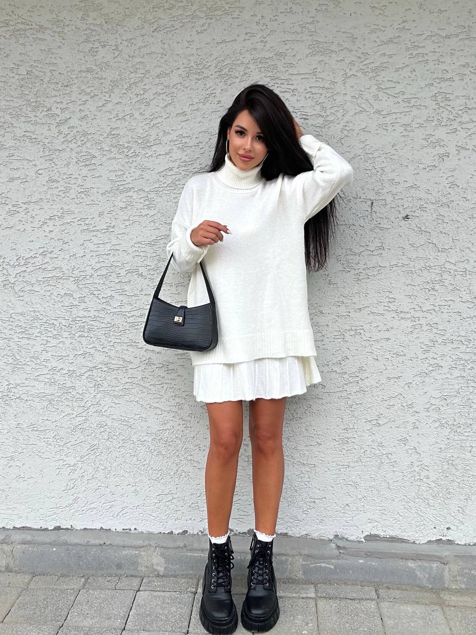Woman in a white outfit with a black bag against a gray wall
