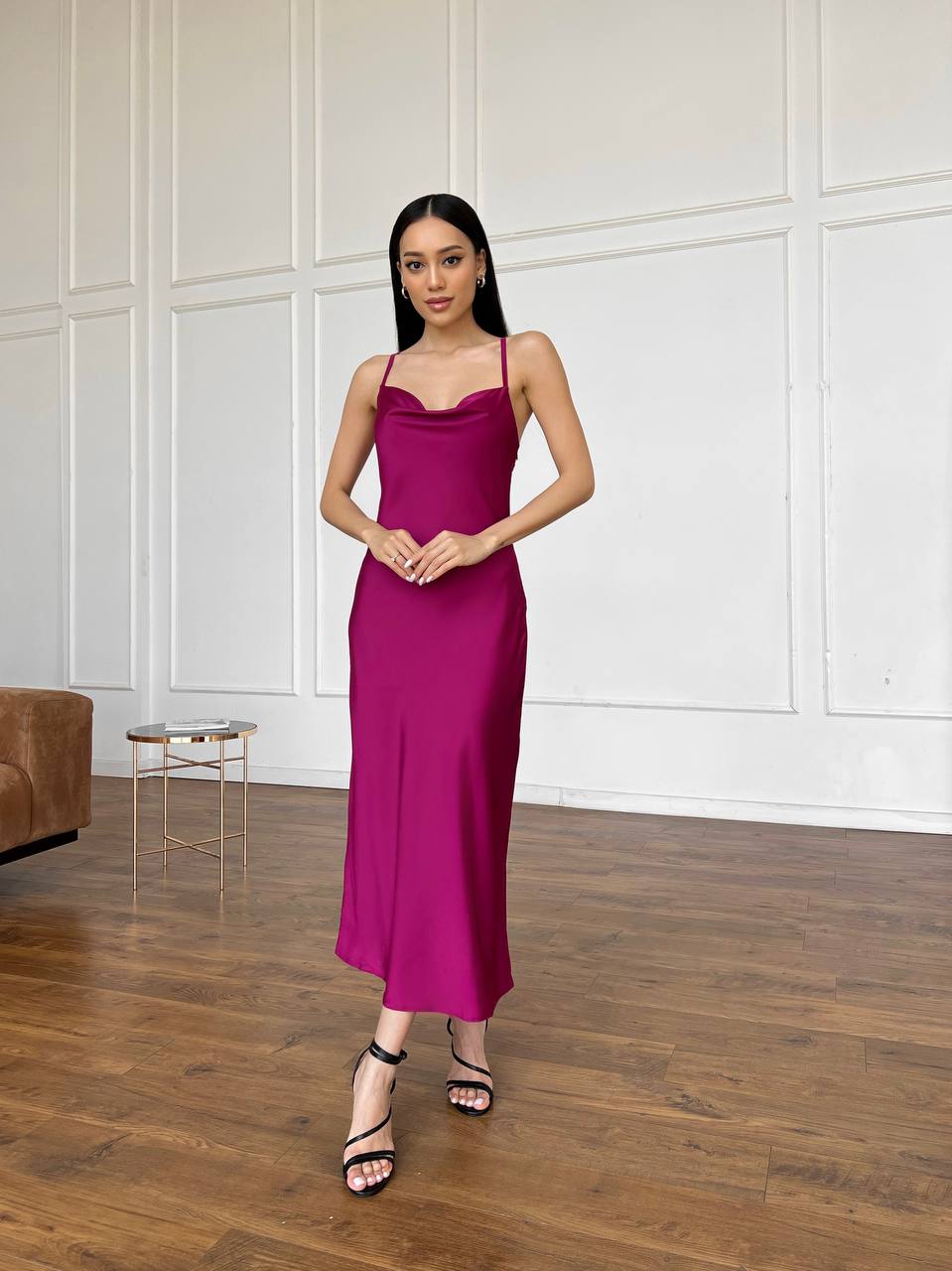 Woman in a pink dress standing in a room with wooden flooring and white paneled walls.
