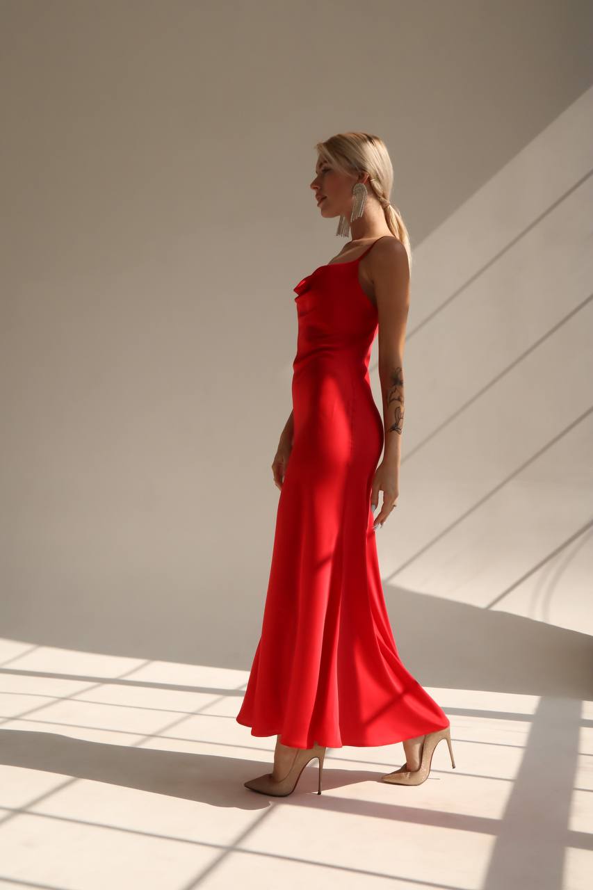 Woman in a red dress standing in a sunlit room with shadows on the wall.