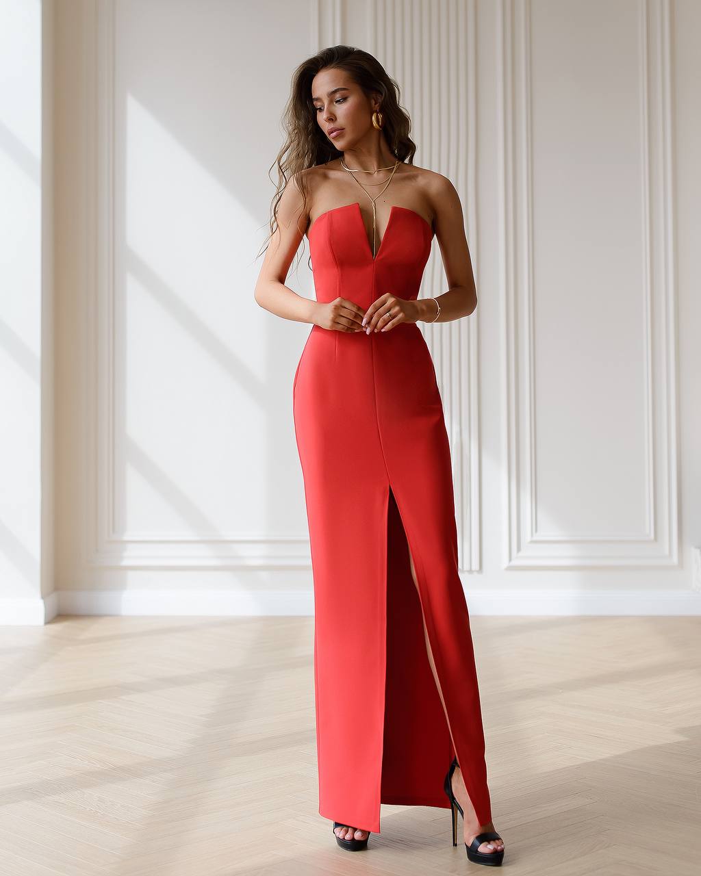 Woman wearing a red strapless gown with a slit in a bright room.