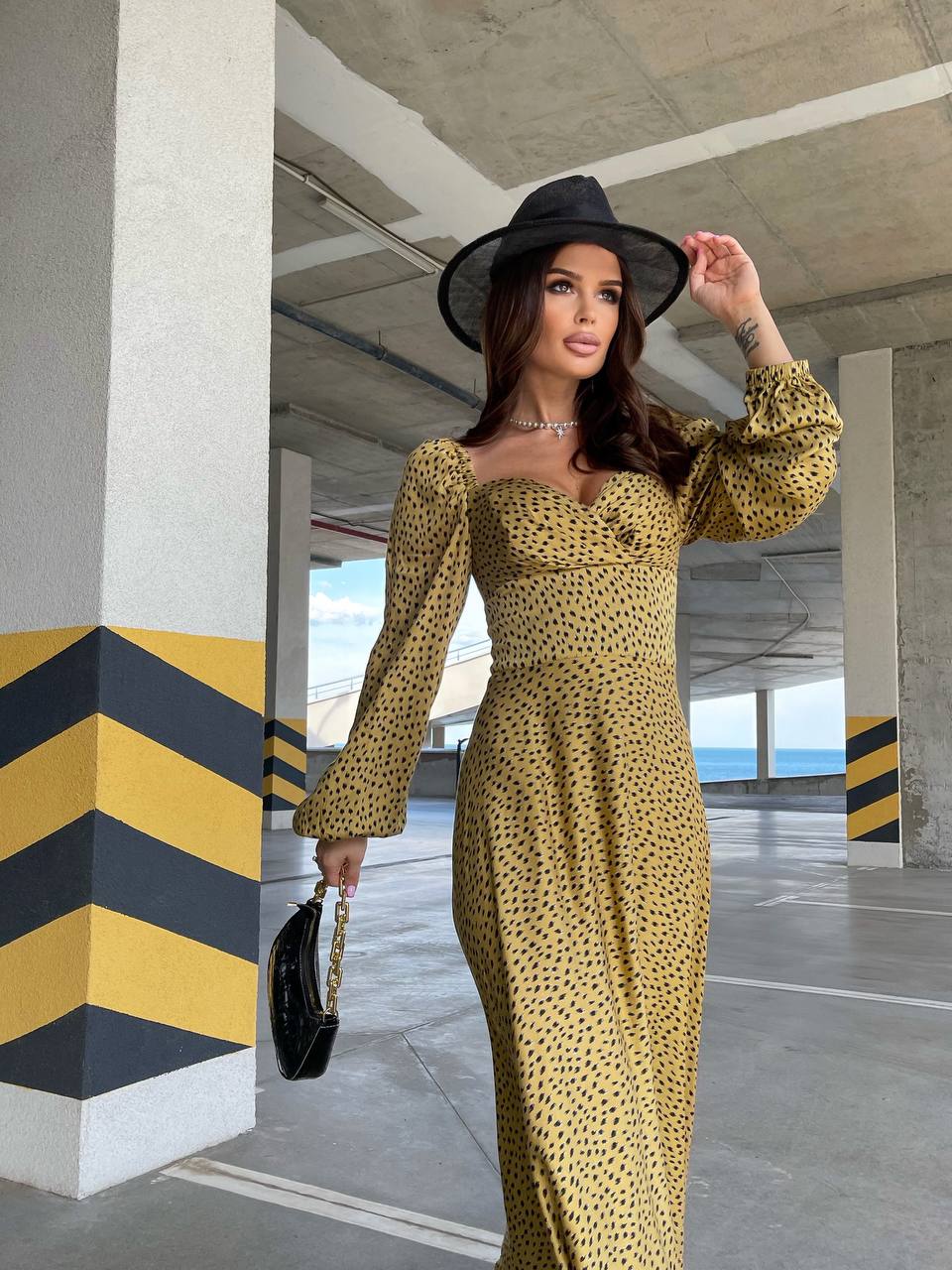 Woman in a yellow dress and black hat standing in an indoor parking garage.
