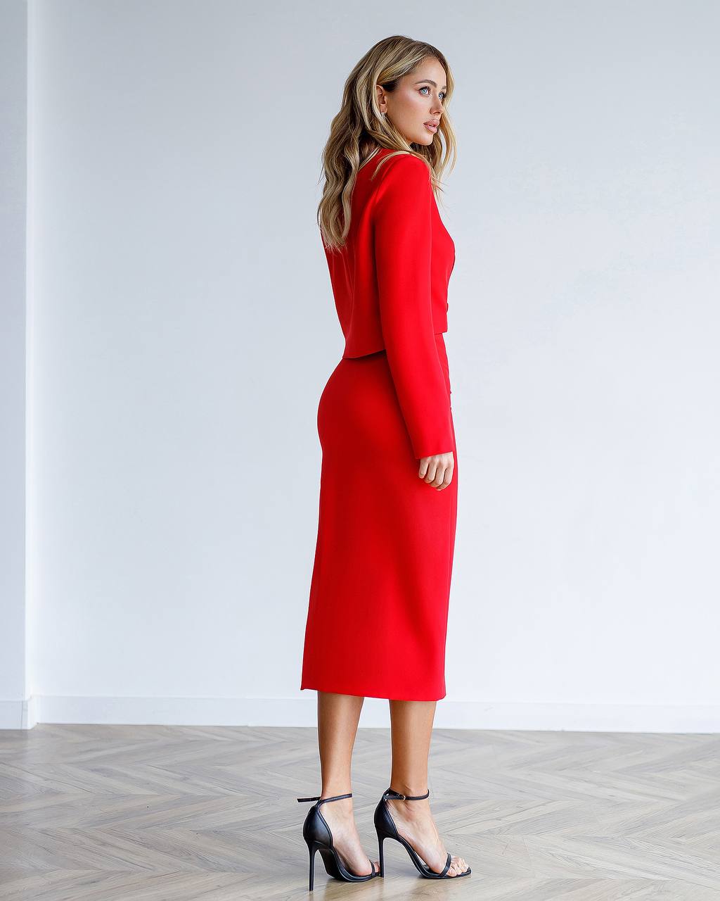 Woman wearing a red dress standing against a white wall.