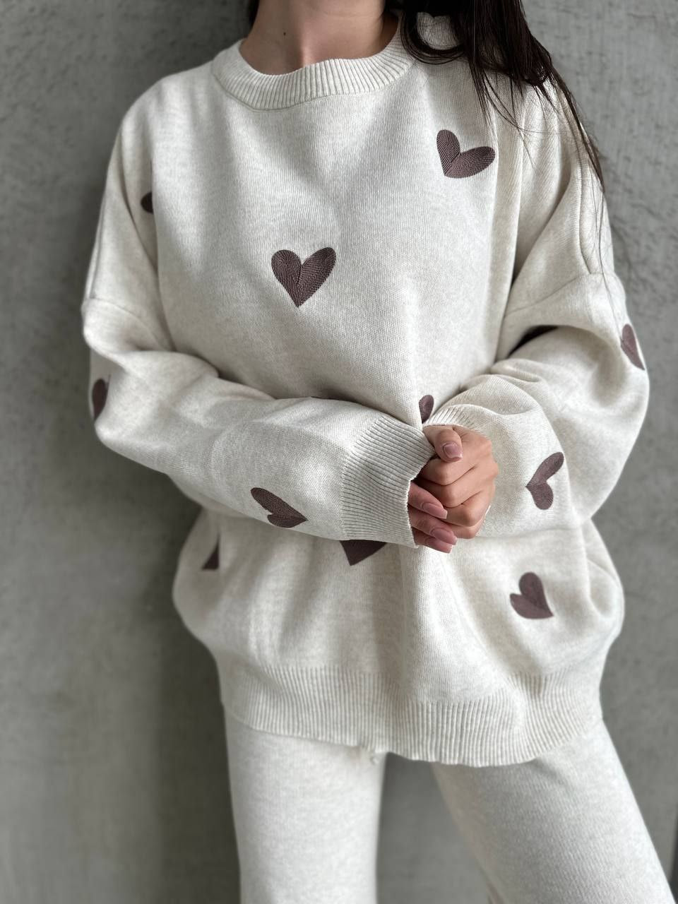 Person wearing a white sweater with brown heart patterns against a gray background