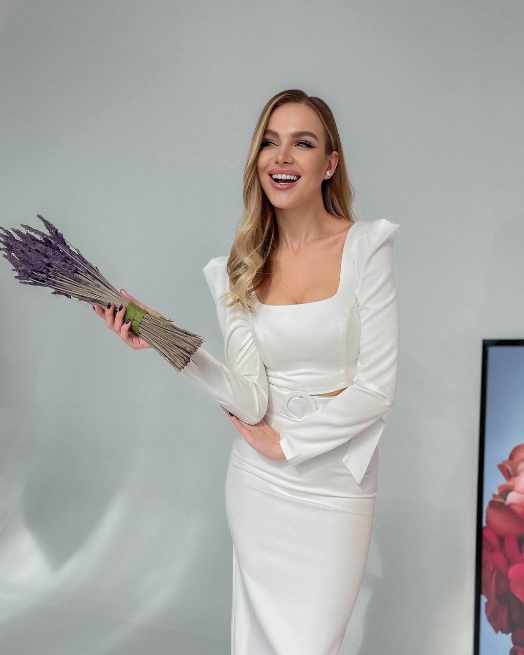 Woman in a white dress holding lavender flowers against a gray background