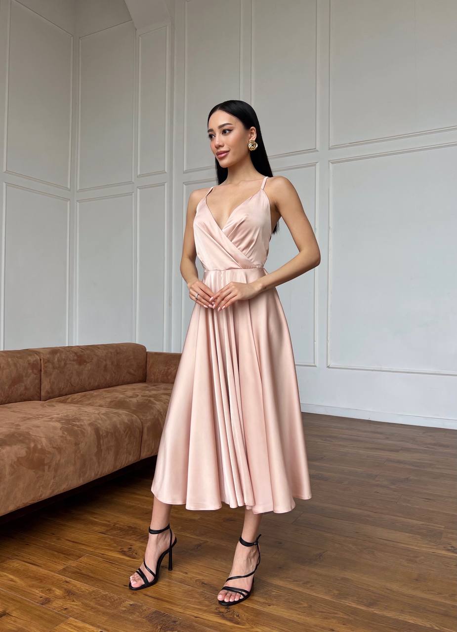 Woman in a pink dress standing in a room with wooden flooring and a brown sofa.