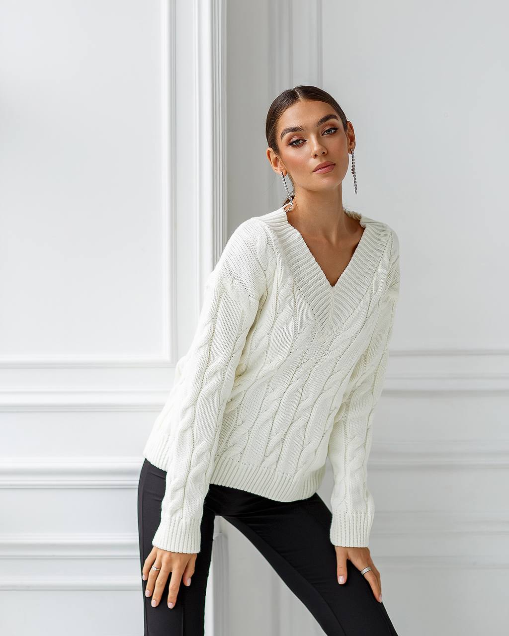 Woman wearing a white cable knit sweater against a light-colored wall.