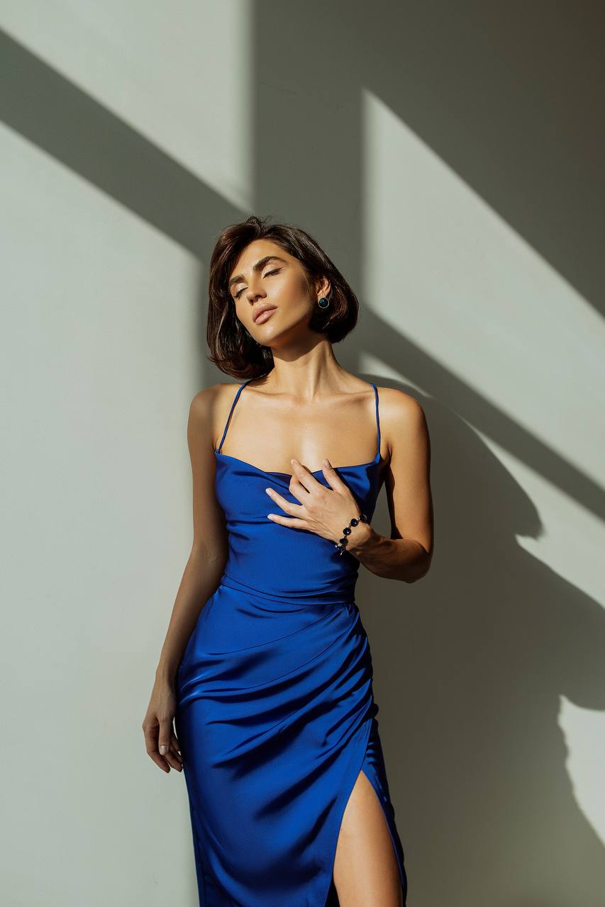 Woman in a blue dress standing against a wall with shadow patterns