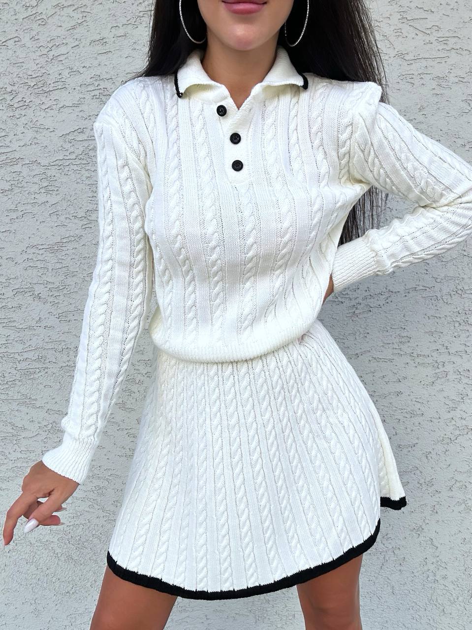 White cable knit dress with black trim against a gray background