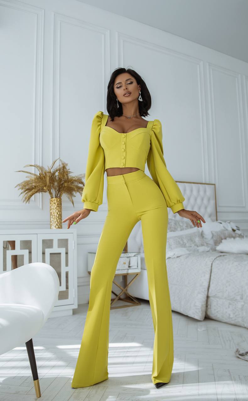 Woman in a bright yellow outfit standing in a stylish room with white walls and decor.