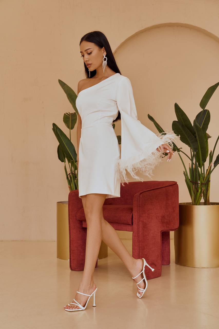 Woman in a white dress standing in a room with plants and a red chair.
