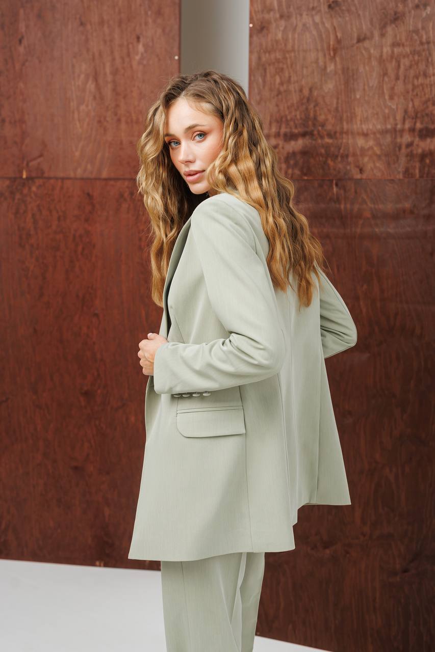 Woman wearing a light green suit against a brown wall