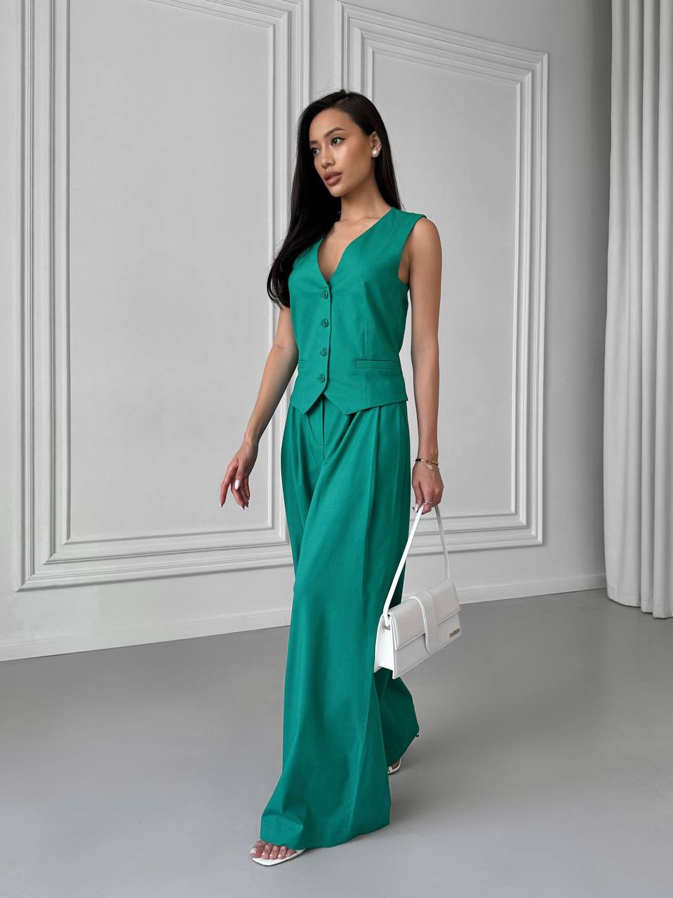 Woman wearing a green jumpsuit in a minimalistic room.