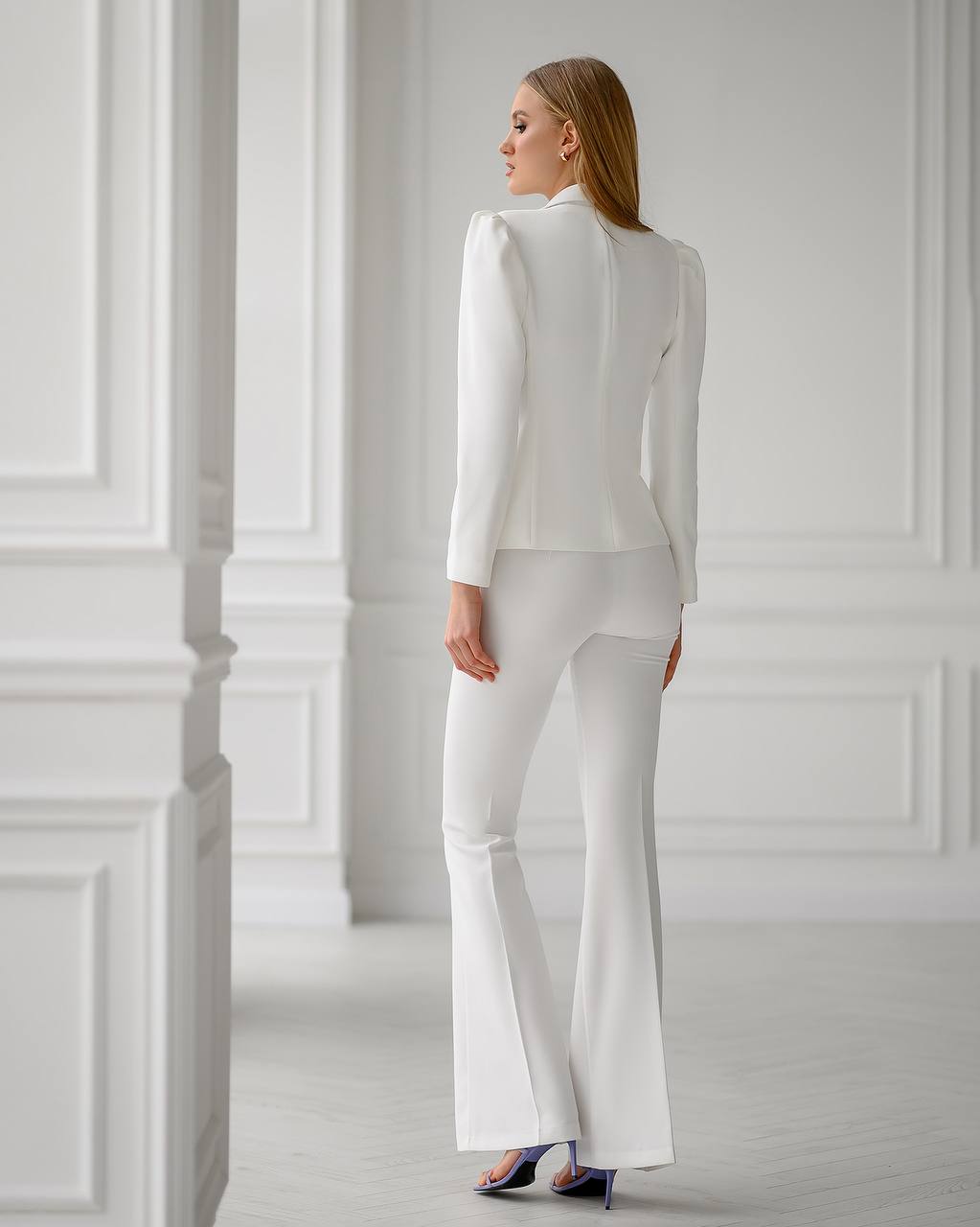 Woman wearing a white outfit standing against a white wall.
