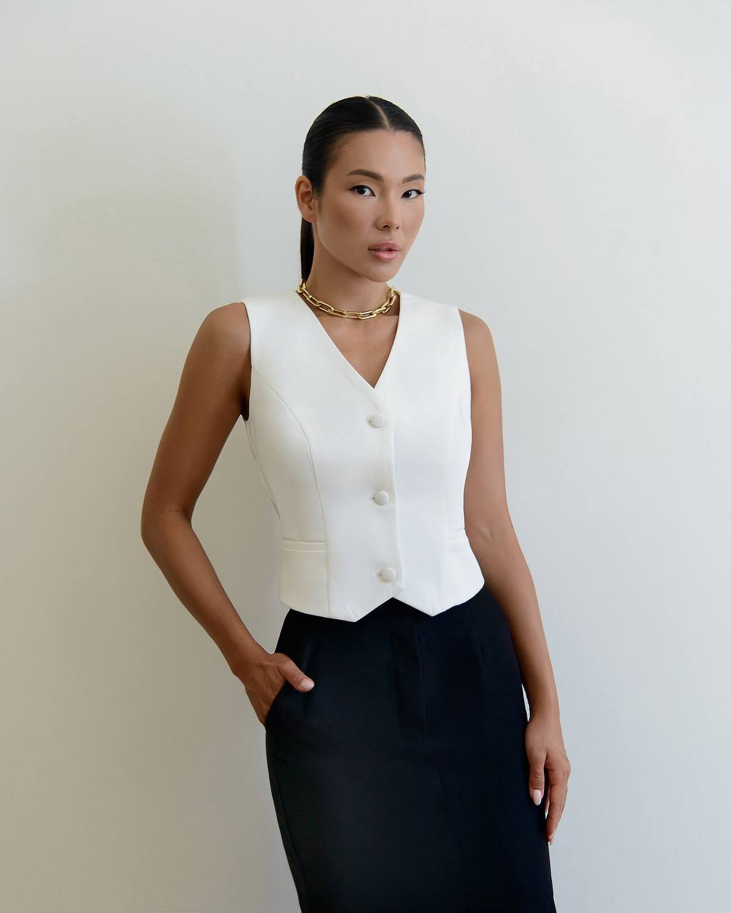 Woman wearing a white sleeveless top and black skirt against a plain background
