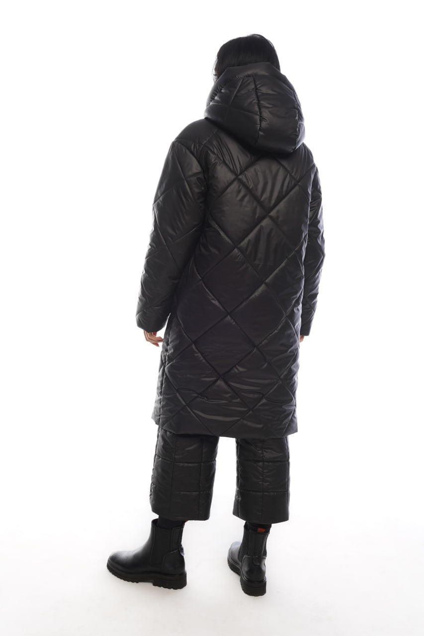Person wearing a long black quilted coat on a white background