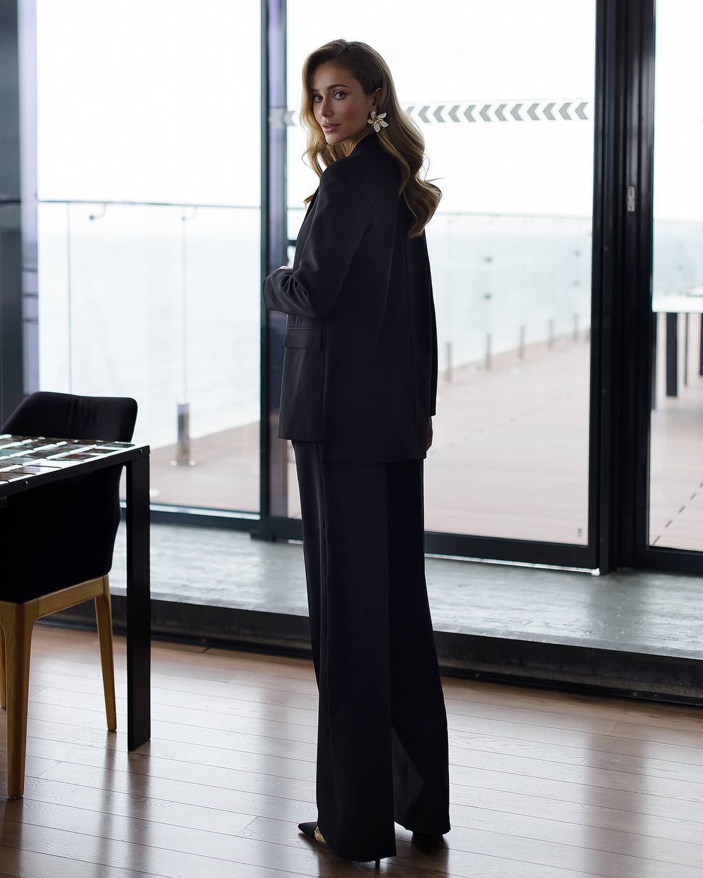 Woman in a black outfit standing in a modern room with large windows.