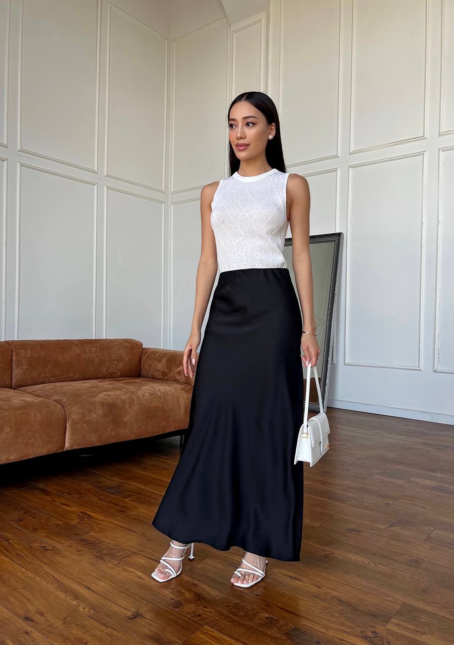 Woman in a white top and black skirt standing in a room with wooden flooring and a brown couch.