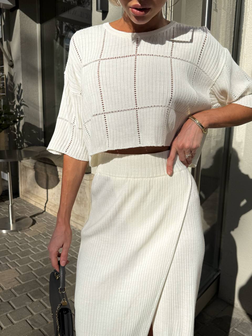 Person wearing a white outfit with a patterned top and skirt, standing outdoors.