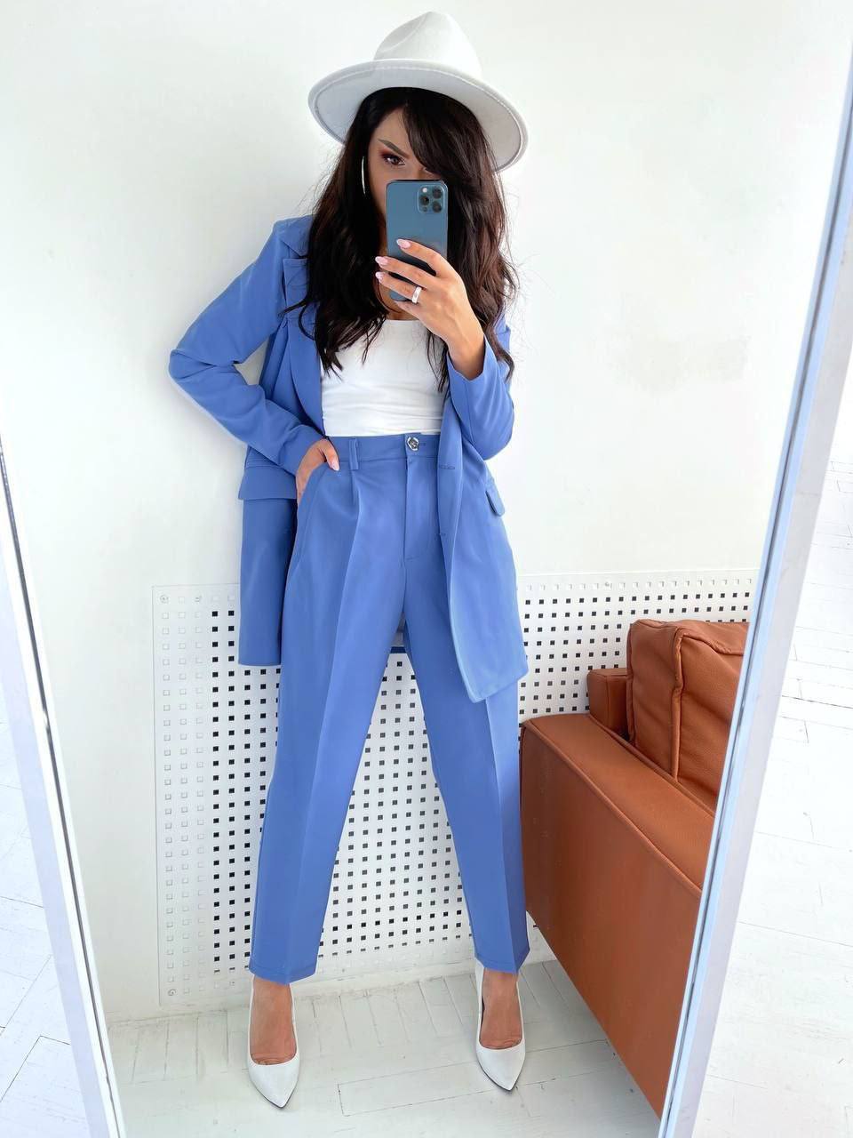Person taking a mirror selfie wearing a blue suit and white hat indoors.