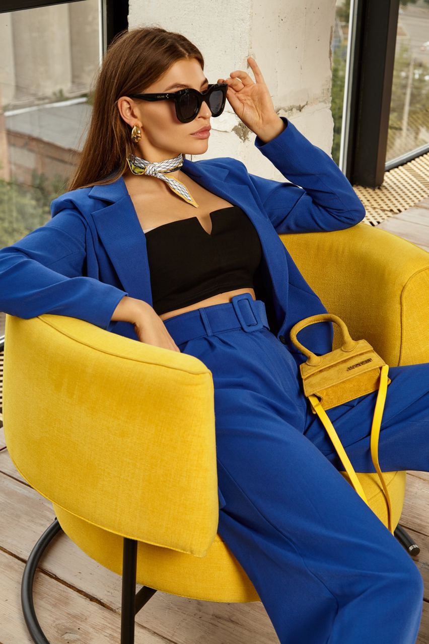 Woman in a blue outfit sitting on a yellow chair with a yellow handbag.