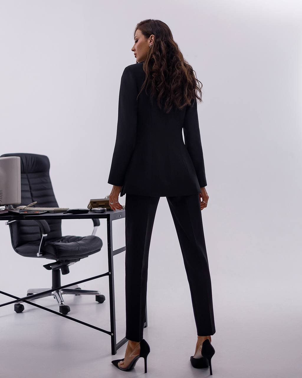 Woman in a black suit standing in an office setting with a white background