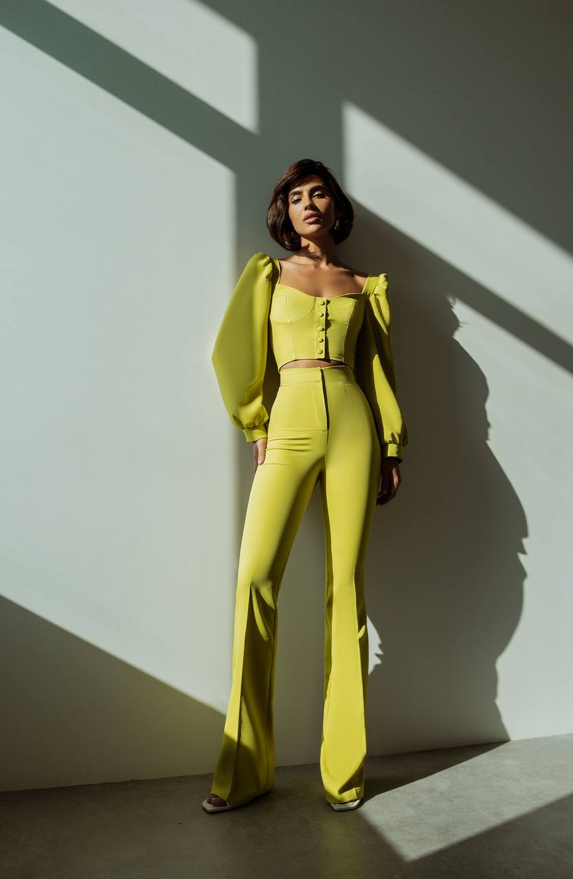 Woman in a bright yellow outfit standing against a white wall with shadows.