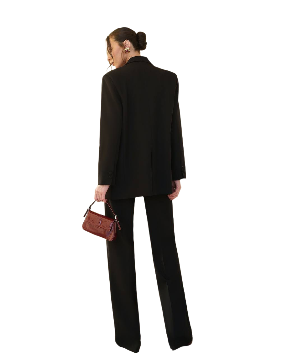 Person wearing a black suit holding a brown handbag on a white background