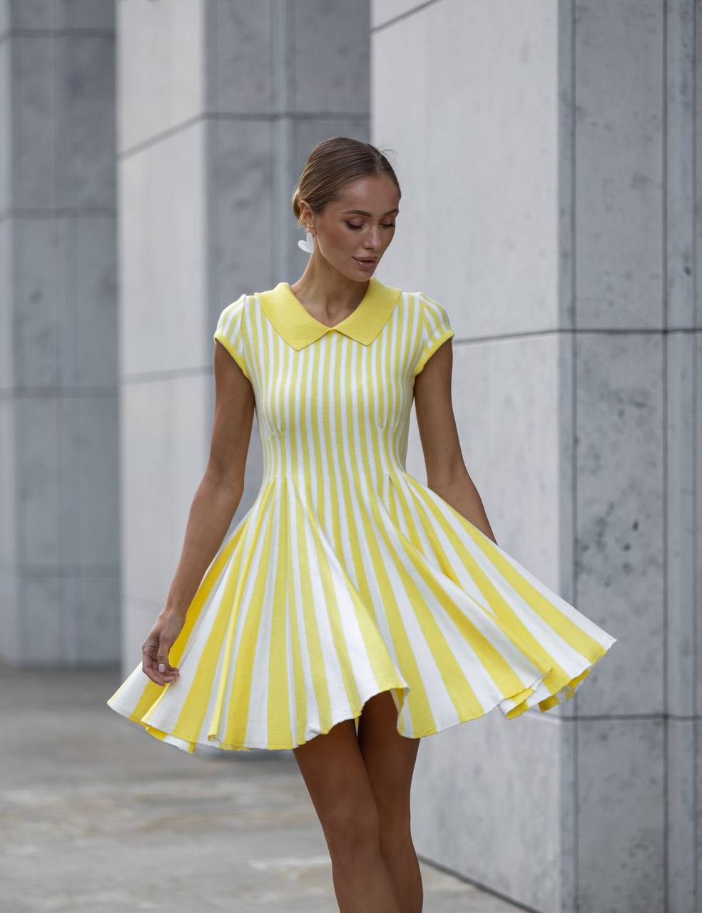Woman wearing a yellow and white striped dress against a gray wall.
