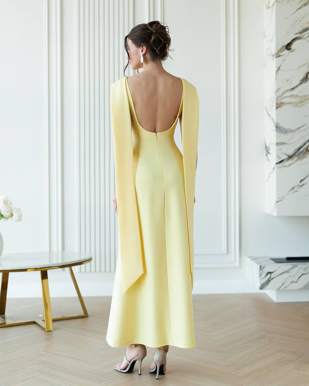 Woman wearing a yellow evening gown with a backless design in an elegant room.