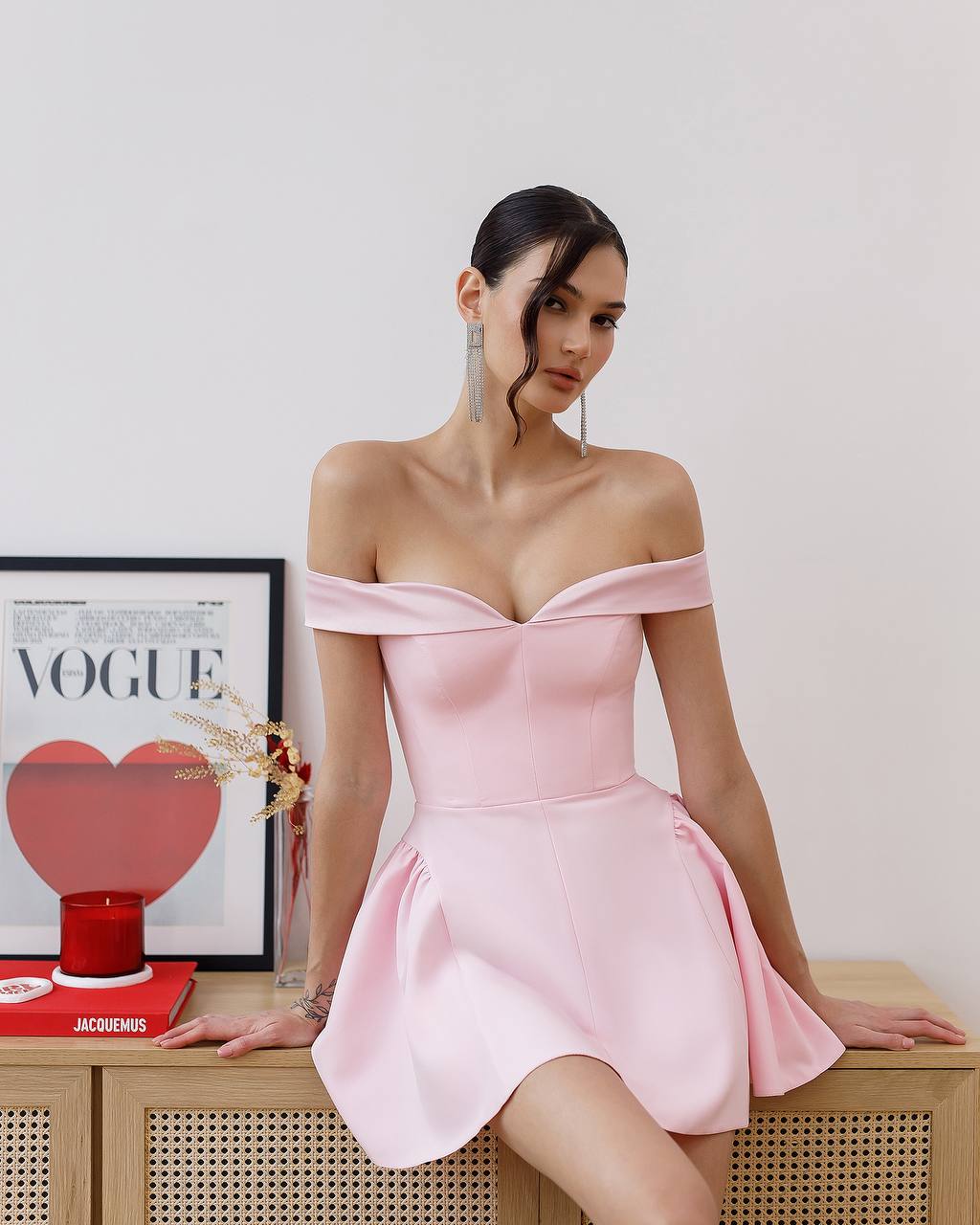 Woman in a pink off-shoulder dress sitting on a wooden surface with a 'Vogue' magazine in the background.