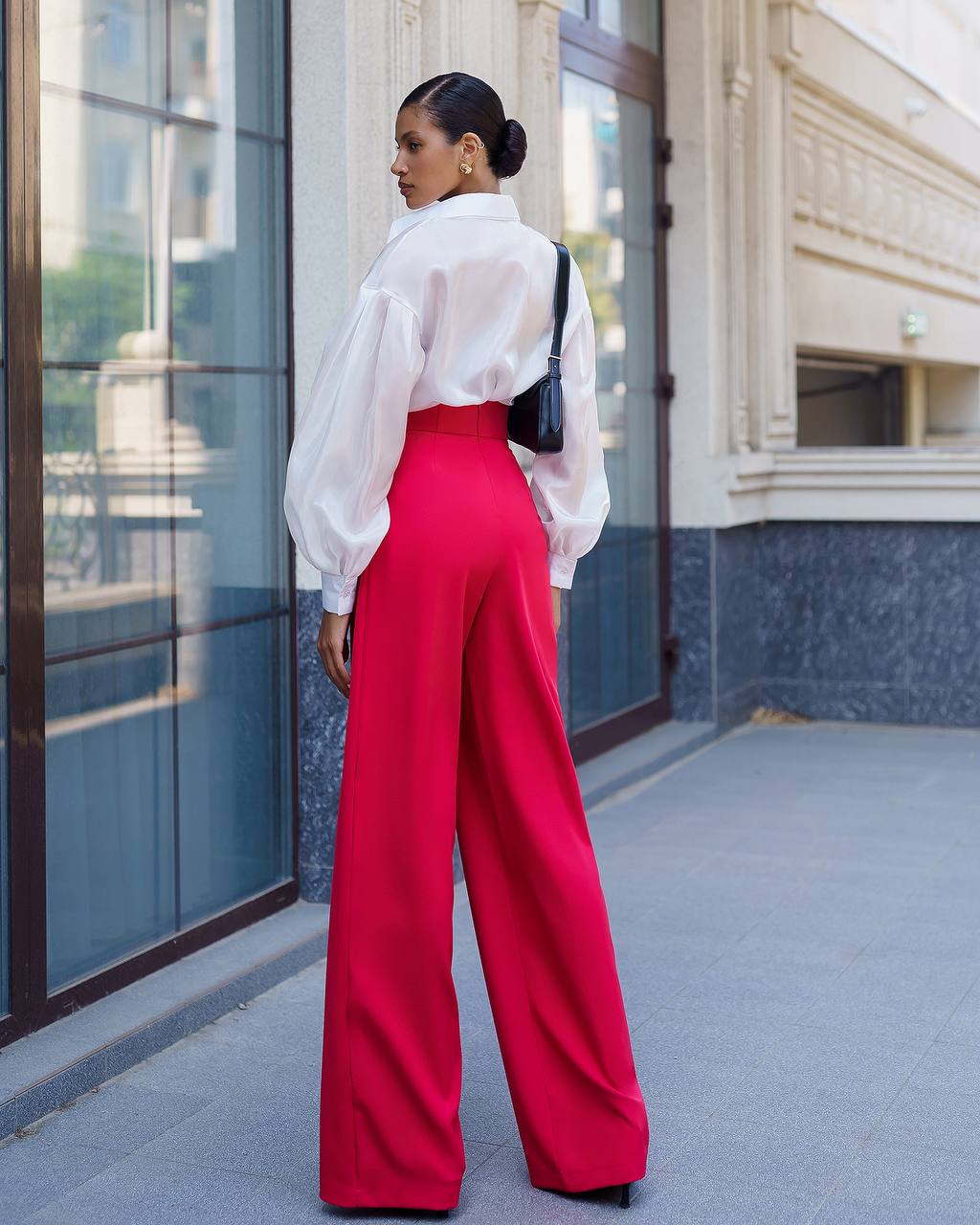 Woman wearing a white blouse and red pants walking past a building.