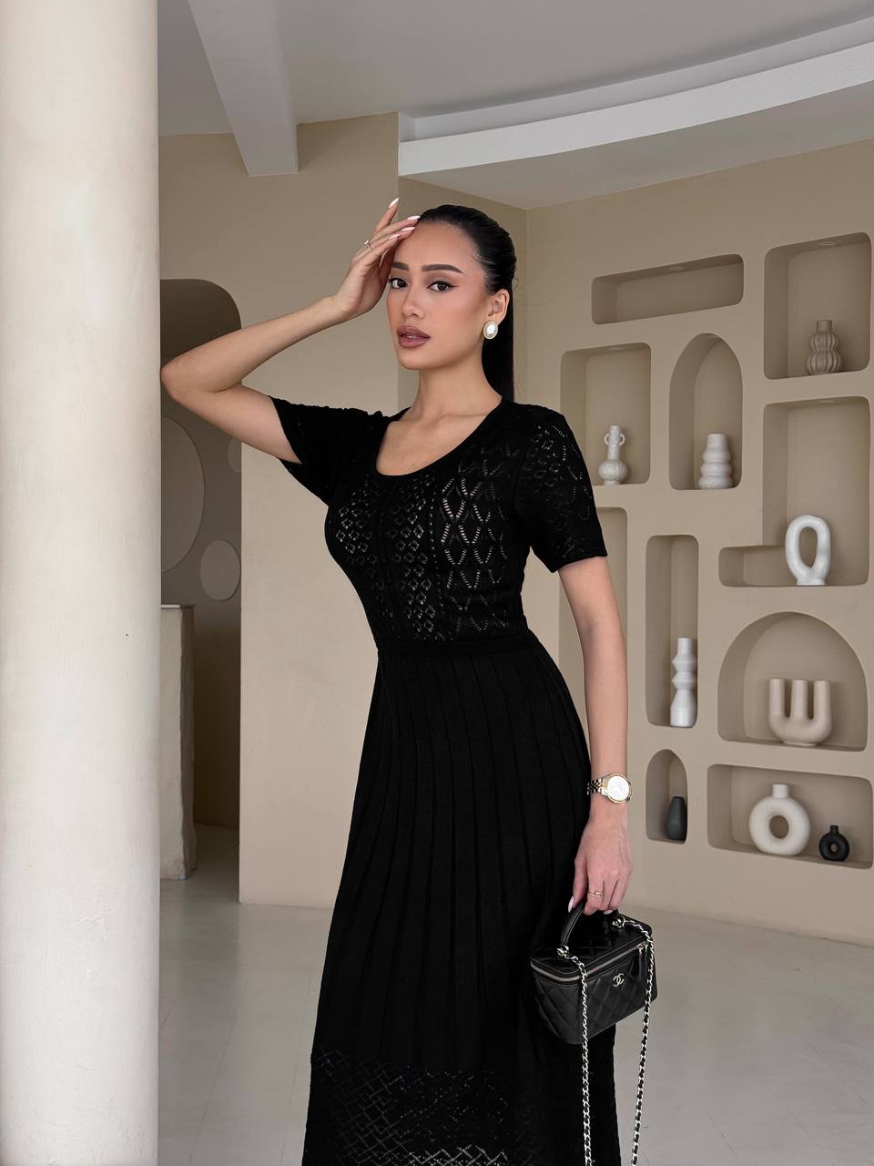 Woman in a black dress posing in an indoor setting with shelves in the background