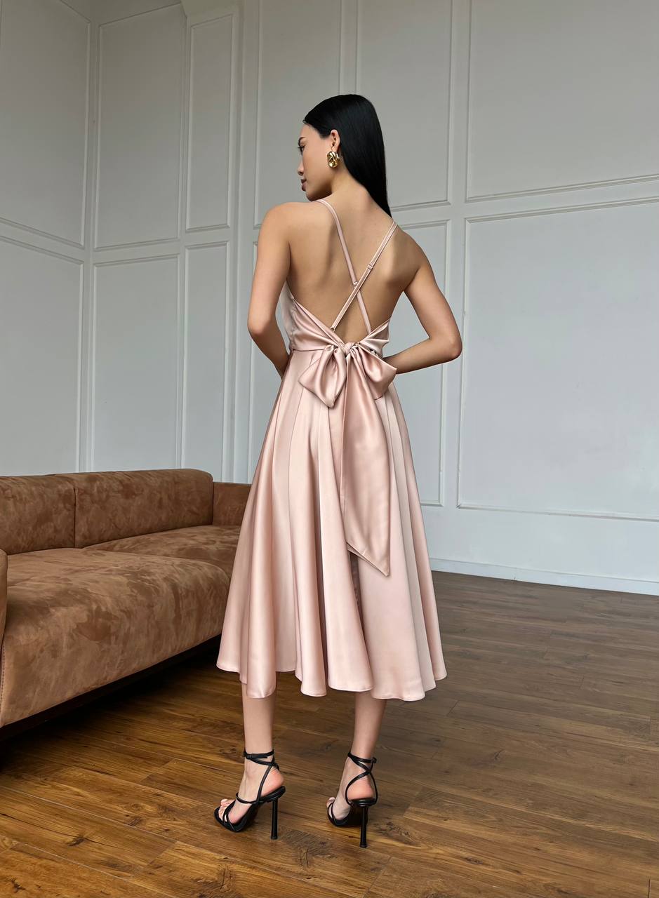 Woman in a pink dress standing in a room with wooden flooring and a brown sofa.